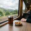新幹線の自席テーブルに置かれたキンキンに冷えた缶ビールと小さなお皿に盛られたおつまみのナッツ