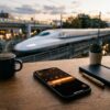 カレンダー画面が表示されたスマートフォンと背後にぼやけて見える高速の新幹線