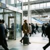 スーツケースを引いて駅の改札出口を笑顔で出る旅行者と背後に見える新幹線